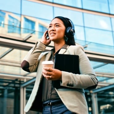 Woman walking with headphones and holding a laptop and coffee